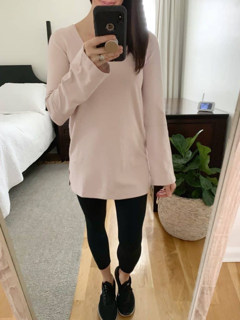 A mirror selfie of a woman wearing a long sleeved creme color sweatshirt and black leggings.