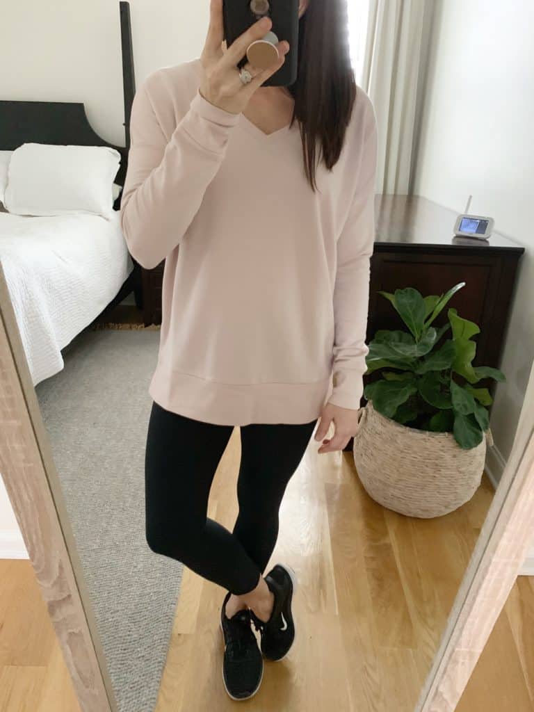 A mirror selfie of a women wearing a light creme colored long sleeve sweatshirt, black capri leggings, and black athletic shoes.