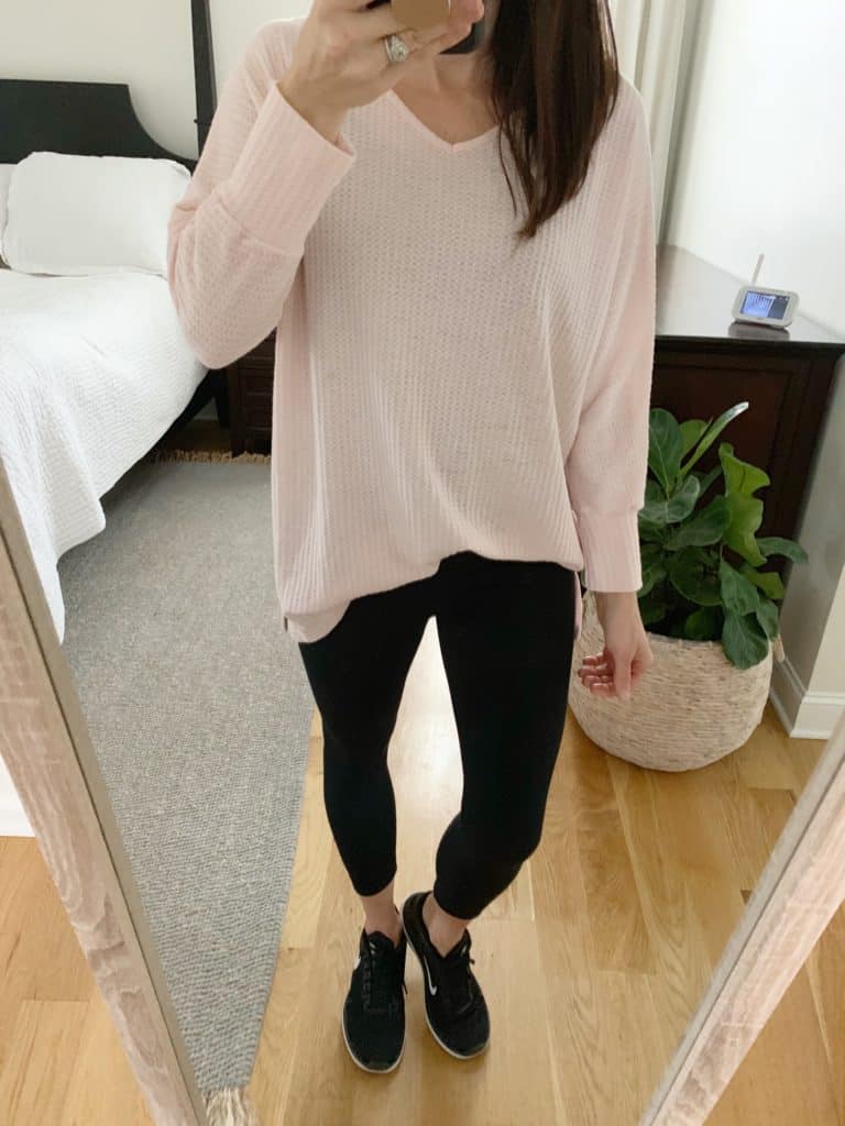 A mirror selfie of a woman wearing a light, long sleeved cream colored shirt, leggings, and black athletic shoes.