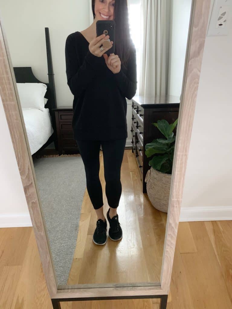 A mirror selfie of a woman wearing a black long sleeved tunic, black leggings, and black athletic shoes.