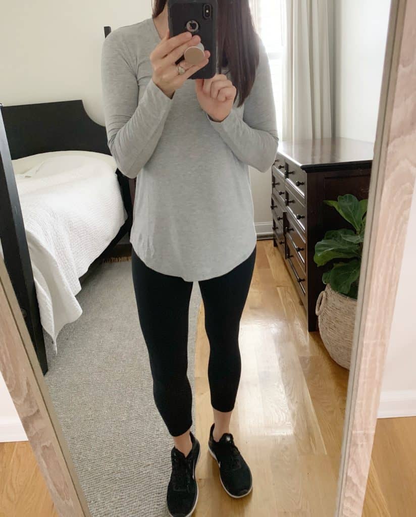 A mirror selfie of a woman wearing a long sleeve gray shirt, black leggings, and athletic shoes.