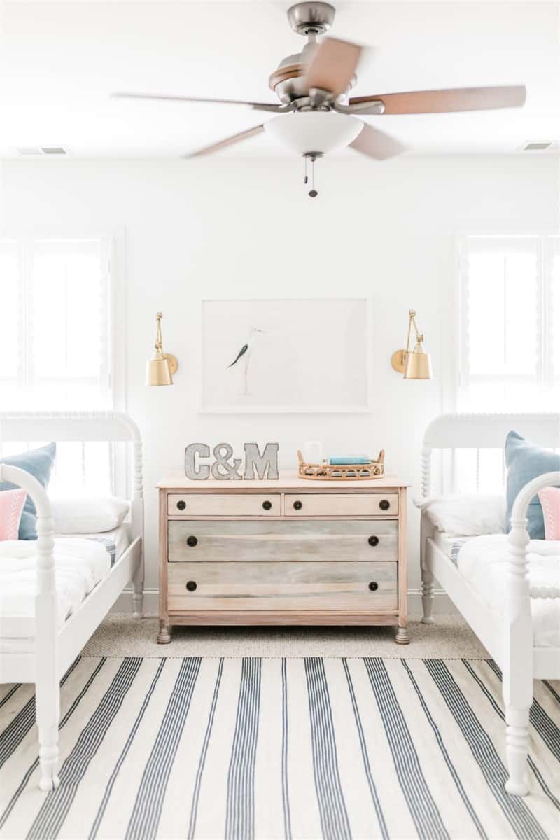 Our kids room, before the spring makeover - the kids room was decorated with all white, spindle beds, a vintage refinished dresser, and white and blue stripped rug.#whitefan #coastalbedroom #kidsroom #sharedroom #hunterfancompany