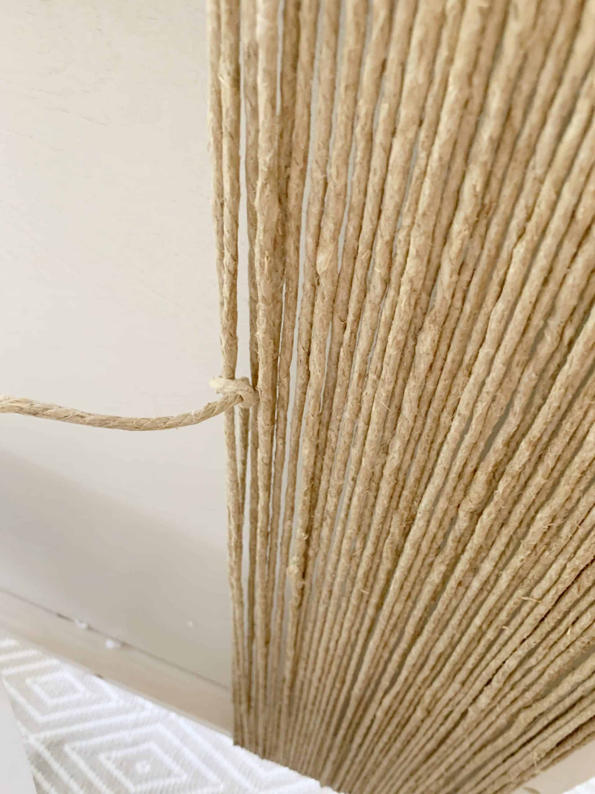 A close up image of wrapped hemp string around the baseboard of my canopy bed. The image shows a knot tied in the string, securing two ends of string together.