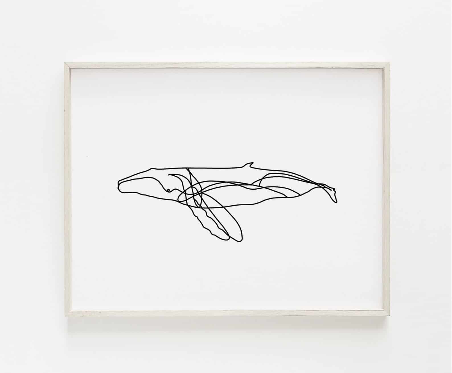 A minimalist line drawing art print shows an abstract whale silhouette against a white background. The coastal art print is framed with a natural wood frame and hangs on a white wall.