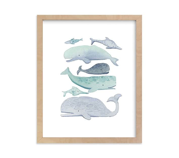 This kid friendly coastal art print features 7 whales of different sizes, all created with watercolors on a white background and framed in a natural wood frame.