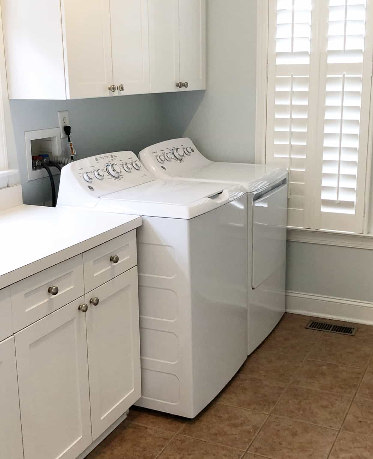 A look at our laundry room before the laundry room makeover - the tile floors were a dark tan tile with light blue walls and a plain countertops