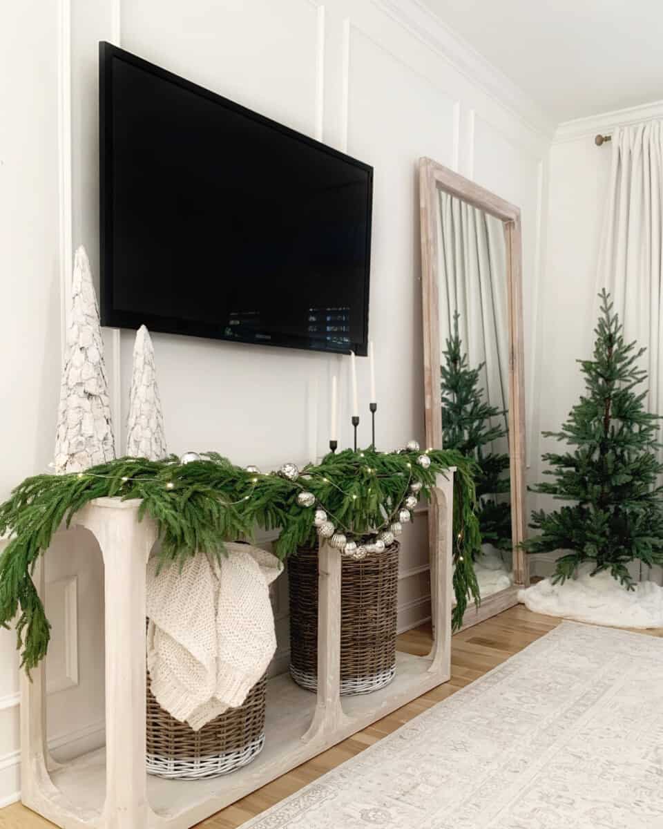 Our master bedroom Christmas decor includes pine garland accented with fairy lights hung over our bedroom TV console, and a mini Christmas tree in the corner of the room.