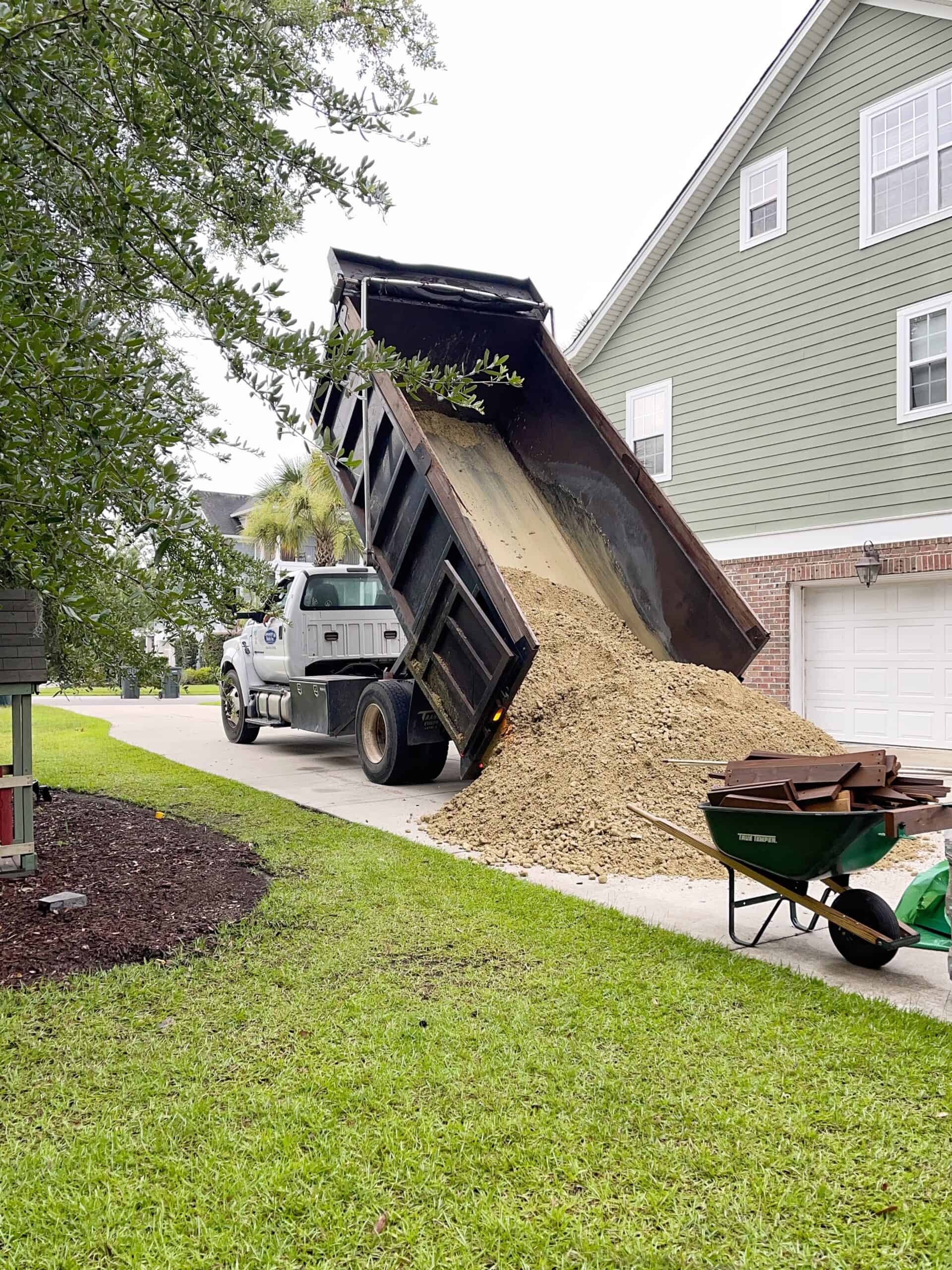 Dump druck in driveway delivering compact material and sand.