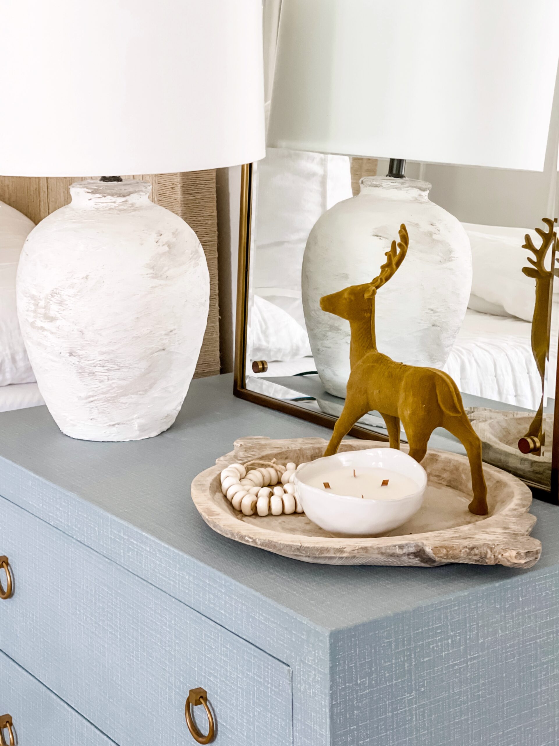 Blue linen covering a chest of drawers with a lamp and mirror.